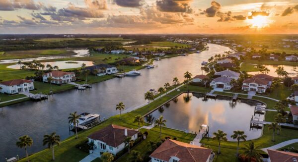 Ultra-realistic 8K aerial photograph of Estero Florida waterfront homes during golden hour showing luxury properties along the Estero River with visible flood zones and retention ponds, dramatic sky, highly detailed