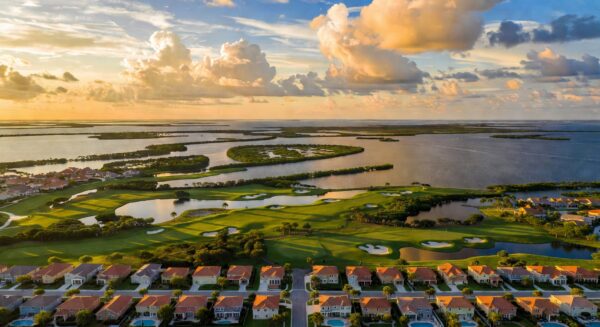 Ultra-realistic 8K aerial photograph of Estero Florida landscape showing master-planned communities, golf courses, and Estero Bay at golden hour with dramatic clouds