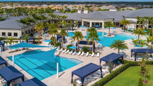 Lifestyle shot of happy active seniors playing pickleball on pristine courts at Bonita Valencia community with the elegant clubhouse visible in the background, sunny Florida day, photorealistic 8K, natural candid moment, premium lifestyle photography