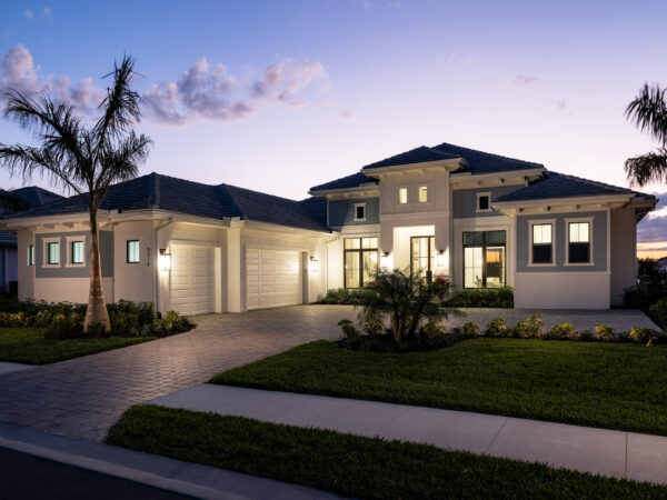 Front elevation of a Caymas Naples custom home at twilight showing sleek contemporary design, tropical landscaping, and elegant driveway approach, museum-quality 8K real estate photography