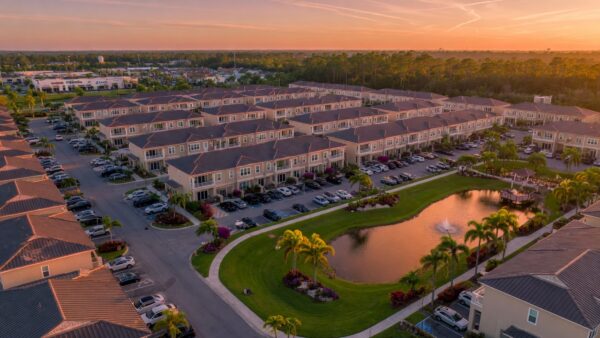 Ultra-realistic 8K aerial photograph of Solis Grande townhome community in Bonita Springs Florida showing tightly arranged modern two-story townhomes with community landscaping and parking areas during golden hour lighting