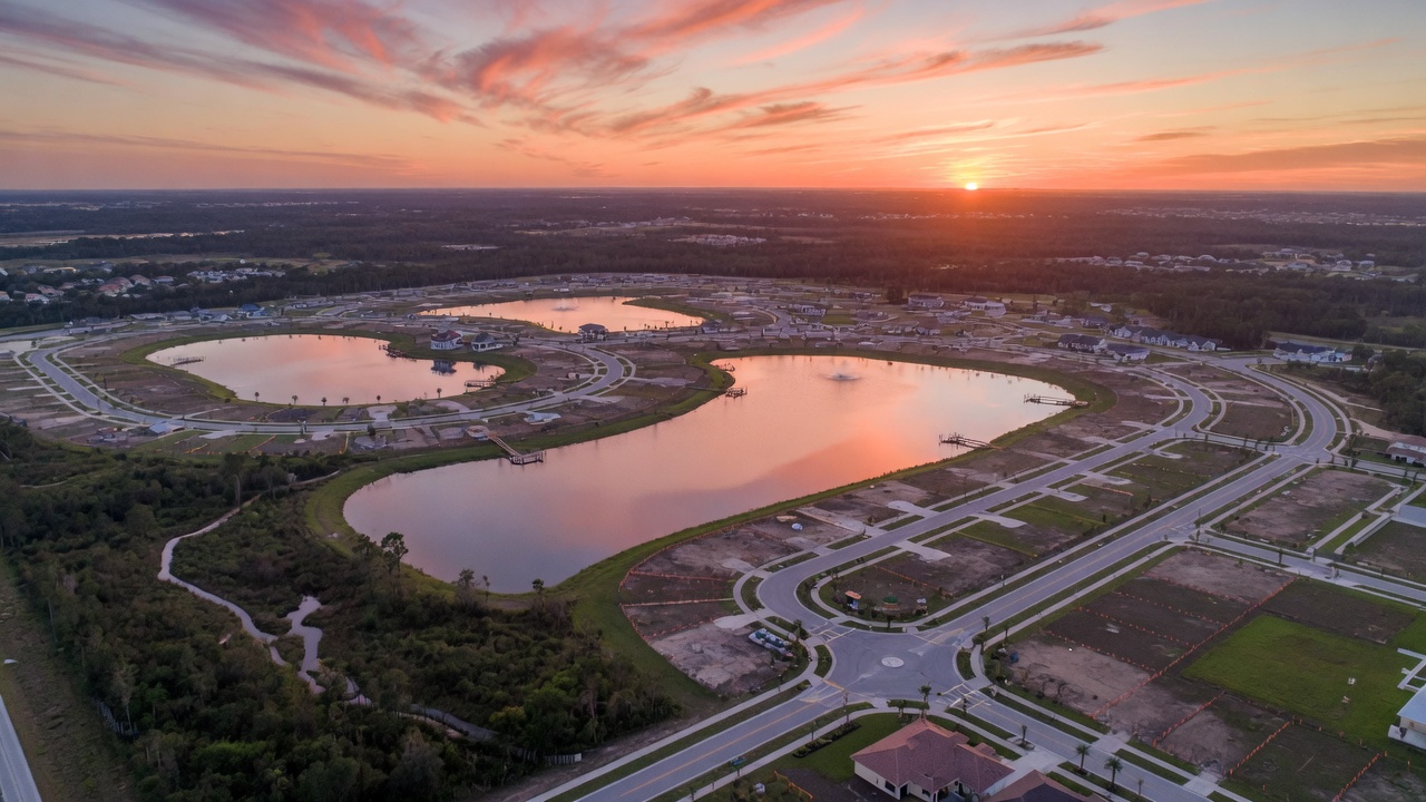 Aerial view of the expansive 1000-acre Vivid Shores master planned community in Bonita Springs showing lakes, preserved natural areas, future homesites and road layout during beautiful sunrise