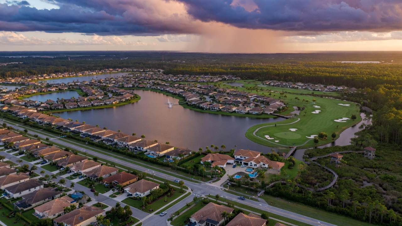 Realistic 8K aerial view of master-planned Estero Florida community showing lakes, golf course, homes and preserve areas with dramatic clouds
