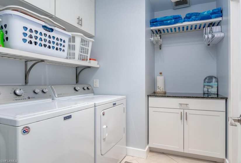 Clothes washing area featuring cabinets, light tile floors, and washing machine and clothes dryer