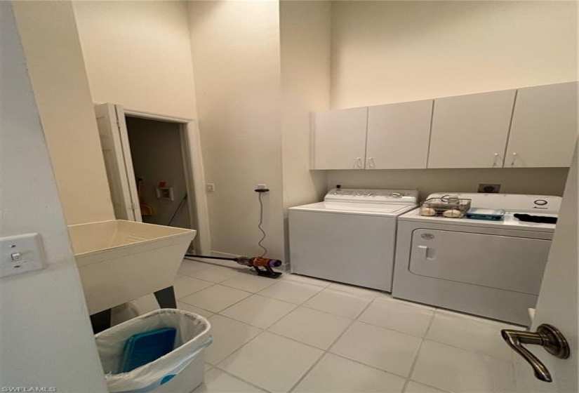 Washroom with washing machine and dryer, hookup for an electric dryer, light tile flooring, and cabinets