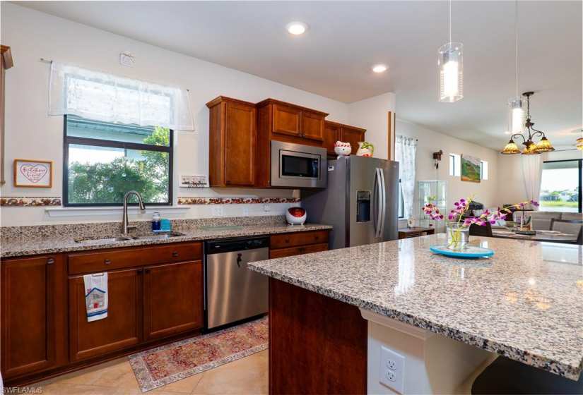 Kitchen with light stone countertops, stainless steel appliances, decorative light fixtures, light tile floors, and sink