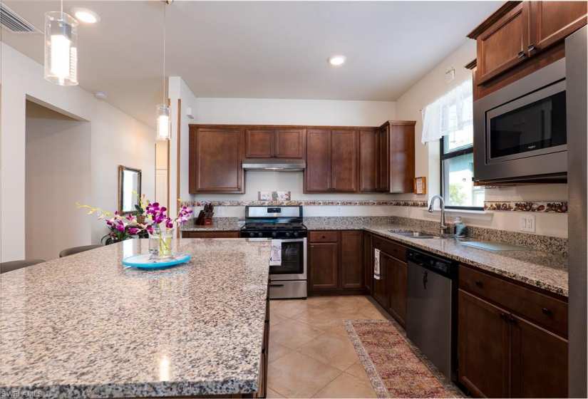 Kitchen with stainless steel appliances, light stone countertops, sink, light tile floors, and pendant lighting