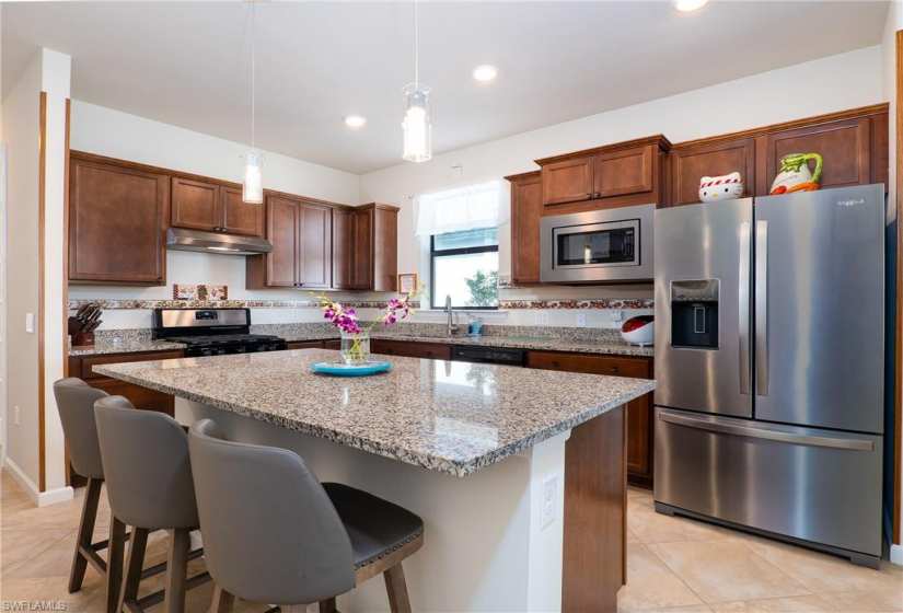 Kitchen featuring decorative light fixtures, appliances with stainless steel finishes, light tile floors, and a kitchen island