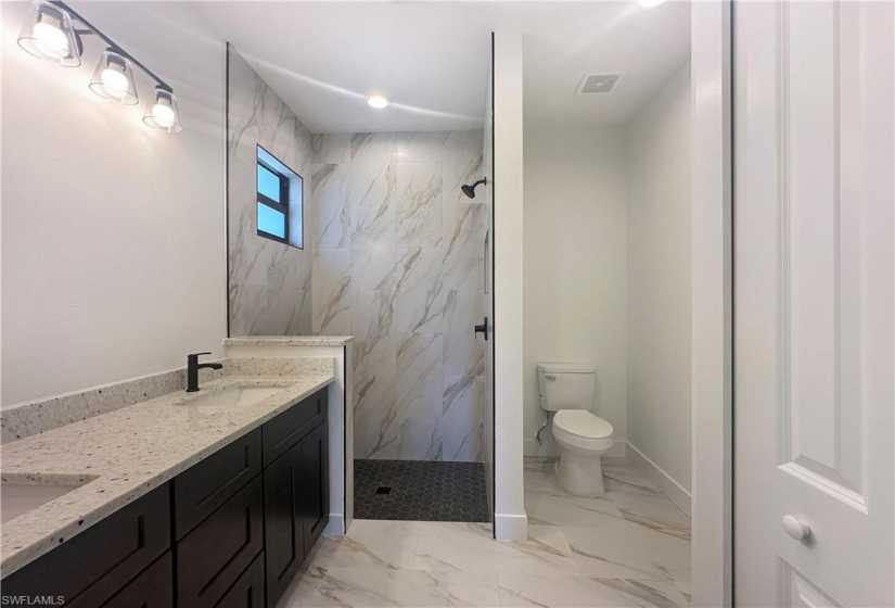 Bathroom with tiled shower, toilet, tile floors, and double vanity