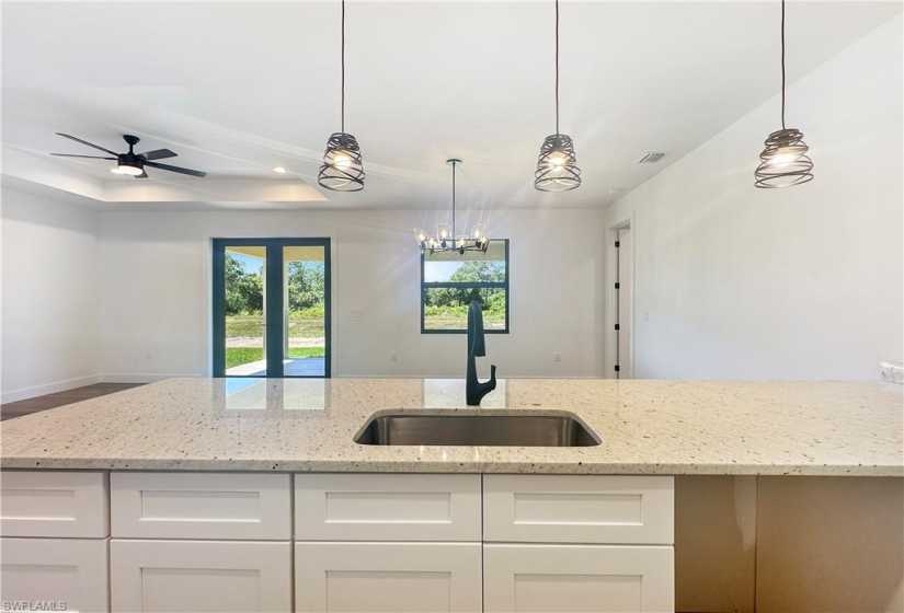 Kitchen featuring sink, white cabinets, light stone counters, and hanging light fixtures