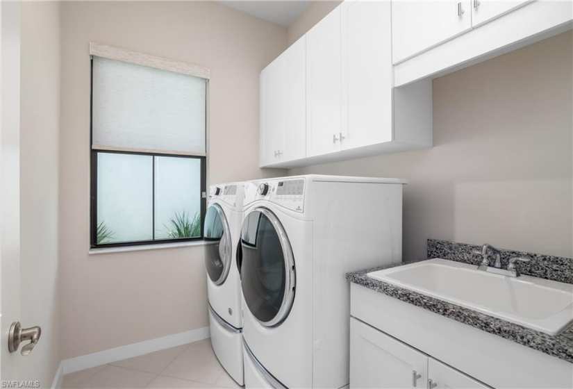 Clothes washing area featuring washer and dryer, cabinets, sink, and light tile floors