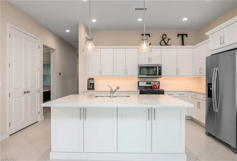 Kitchen featuring hanging light fixtures, stainless steel appliances, a center island with sink, and light tile floors