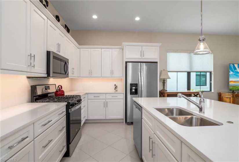 Kitchen featuring white cabinets, light tile flooring, stainless steel appliances, sink, and pendant lighting