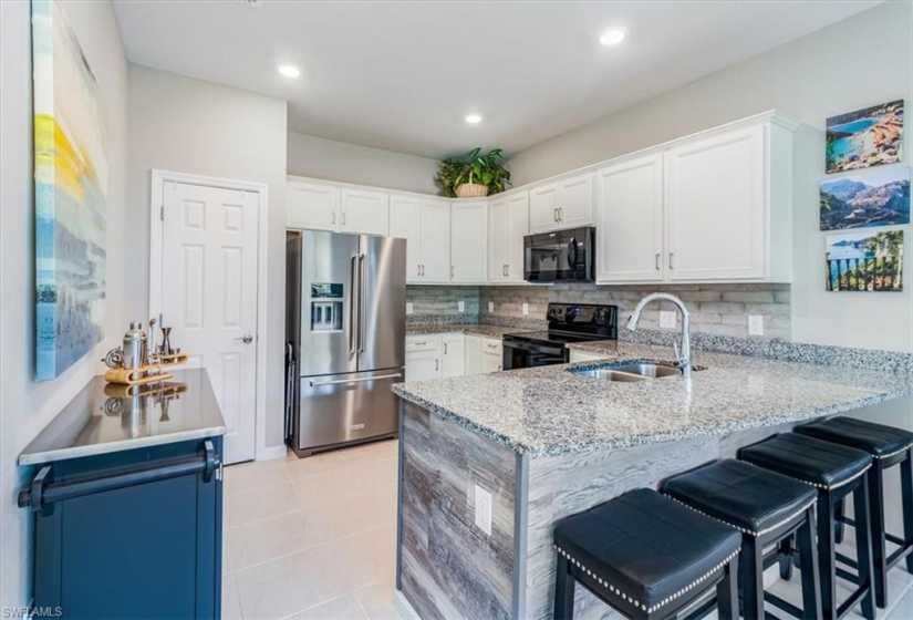 Kitchen featuring kitchen peninsula, tasteful backsplash, black appliances, sink, and light tile floors