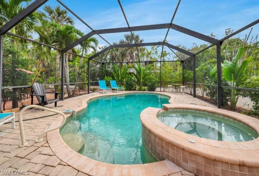 Large heated pool with spa completely enclosed by a sturdy pool cage.