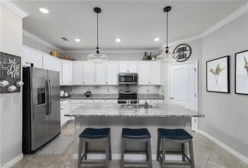 The kitchen features a walk-in pantry, granite counters and a custom beveled subway tile backsplash, stainless steel appliances, recessed lighting and pendant lights over the breakfast bar.