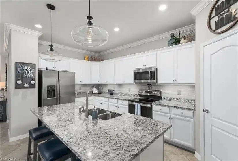 The kitchen features a walk-in pantry, granite counters and a custom beveled subway tile backsplash, stainless steel appliances, recessed lighting and pendant lights over the breakfast bar.