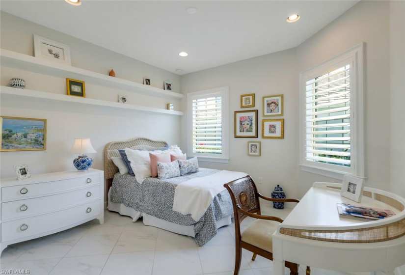 Private guest bedroom with decorative custom shelving detail and plantation shutters.